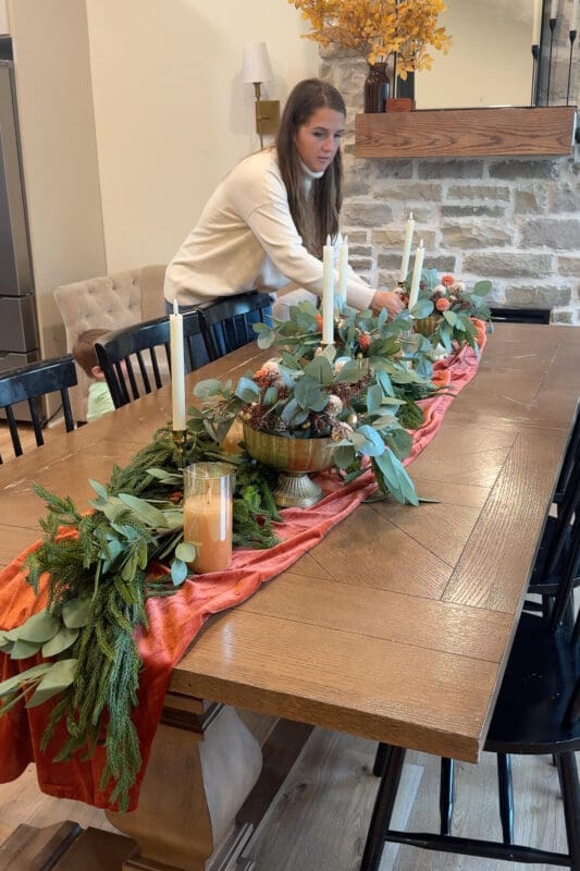 Placing brass bowl centerpieces filled with faux mums along the garland on a Thanksgiving table